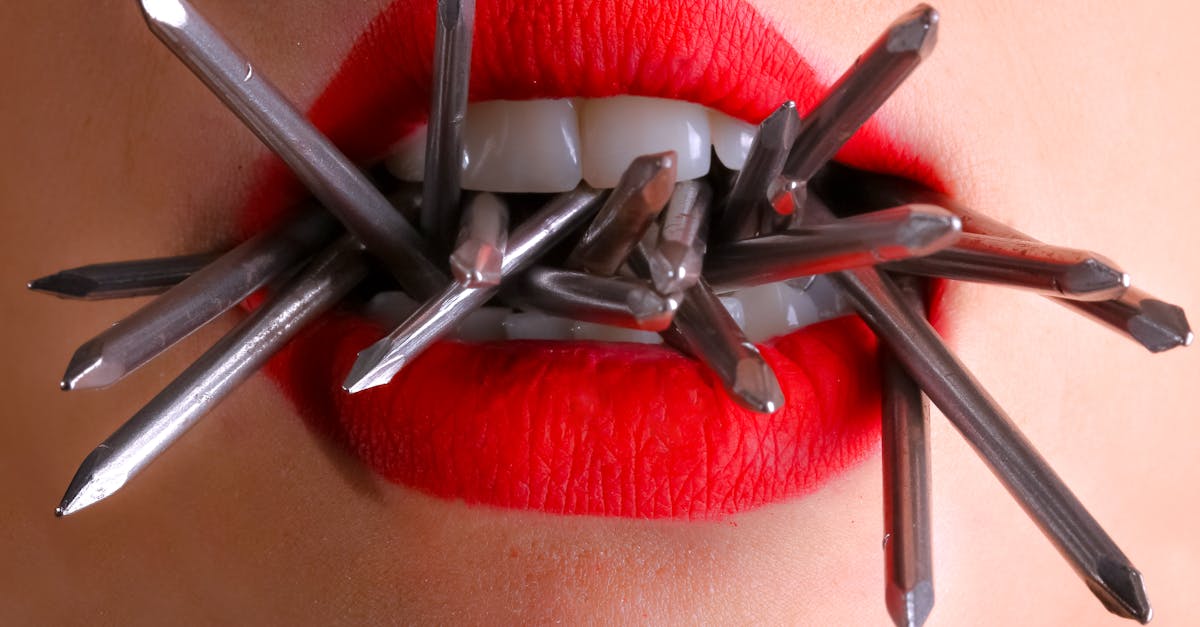 Artistic close-up of red lips biting metal spikes, contrasting beauty and strength.