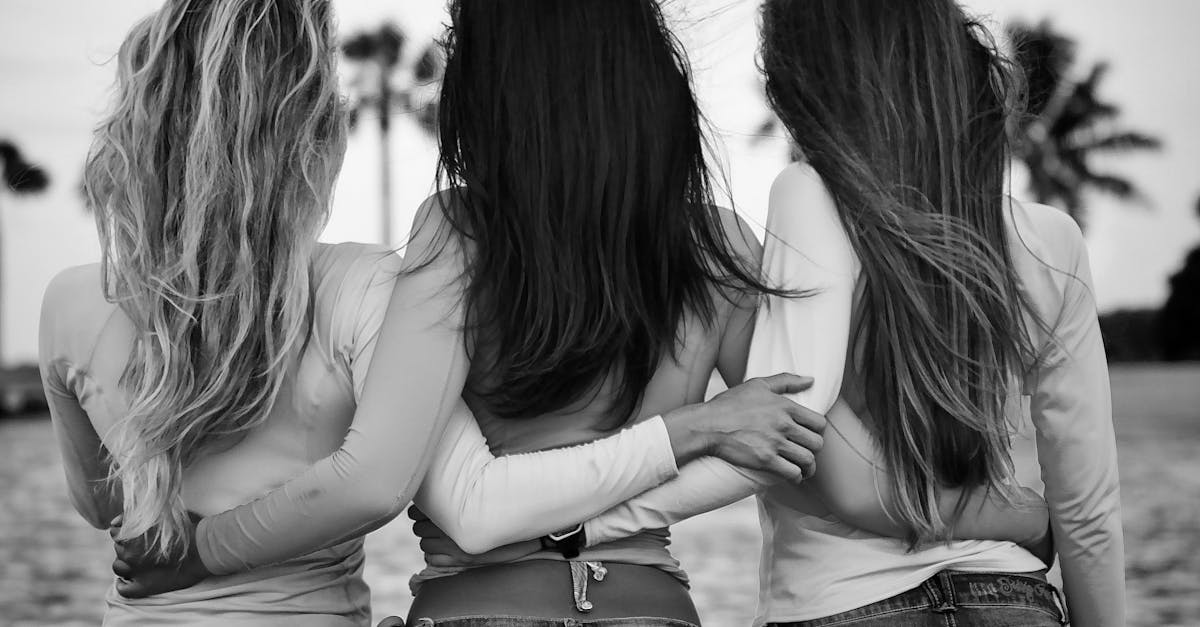 Three women in jeans and tops bonding at the beach in grayscale.