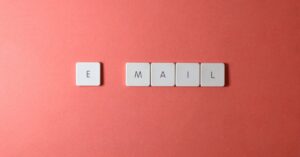 Flat lay of keyboard letter tiles spelling 'email' on coral backdrop.