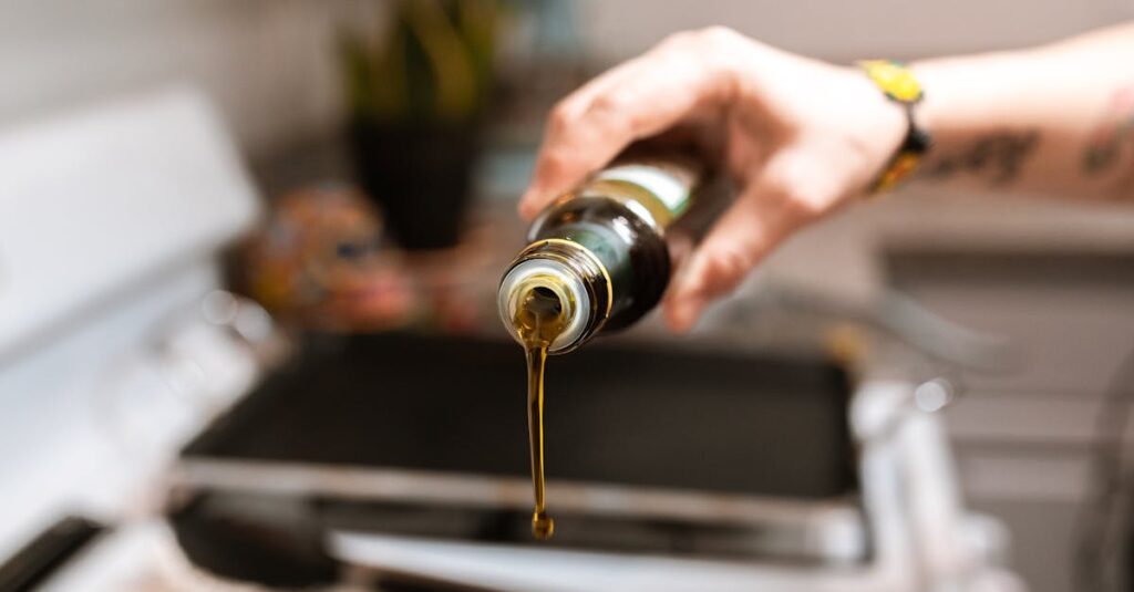 A focused image showing olive oil being poured from a bottle into a pan during cooking.