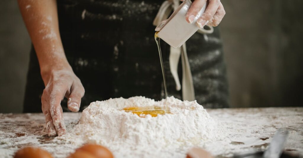 Chef pouring oil into flour and egg mix for homemade pasta.