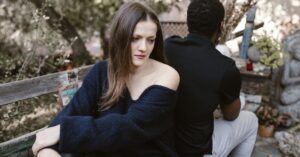 A couple sits on a bench back-to-back, conveying sadness and separation outdoors.