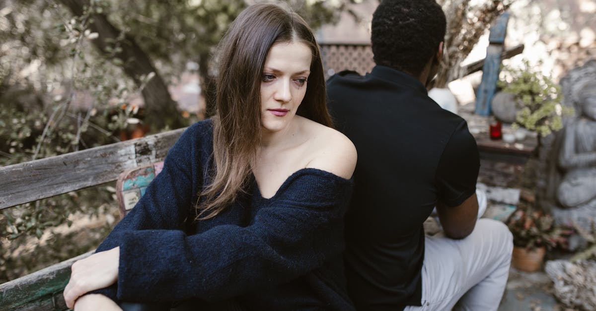 A couple sits on a bench back-to-back, conveying sadness and separation outdoors.