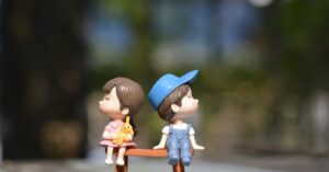 Adorable figurines of a boy and girl sit on a bench, bathed in summer sunlight.